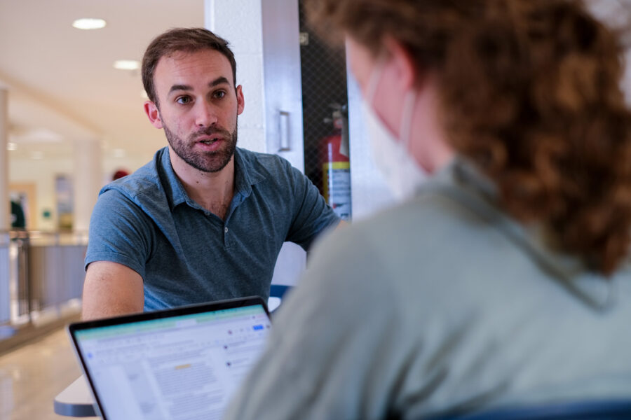 male sitting at a table looking at a female across the table; a laptop is on the table between them