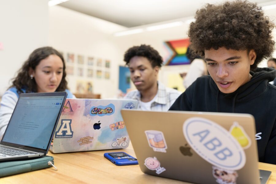 three high school students sitting at desks and looking at computers