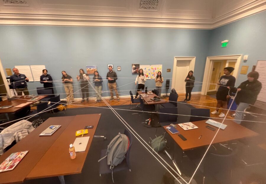 students and a teacher standing in a classroom stretching a string from person to person