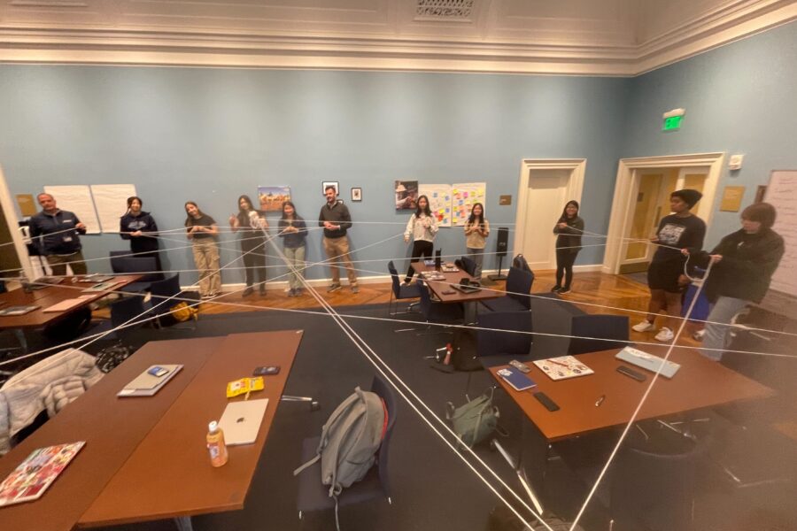 students and a teacher standing in a classroom stretching a string from person to person