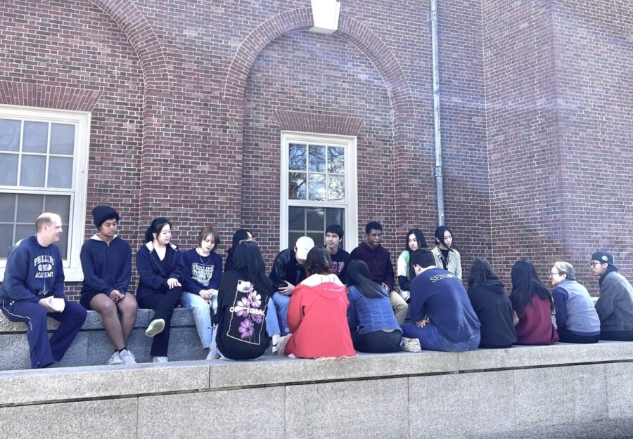 20 students and faculty sit outside near a brick wall