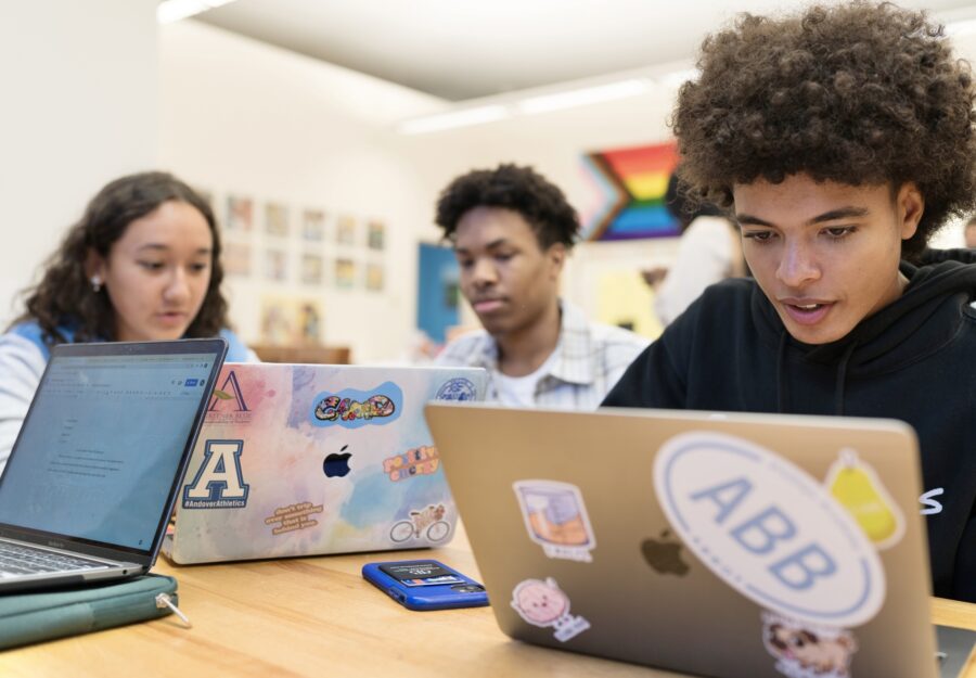 three high school students sitting at desks and looking at computers