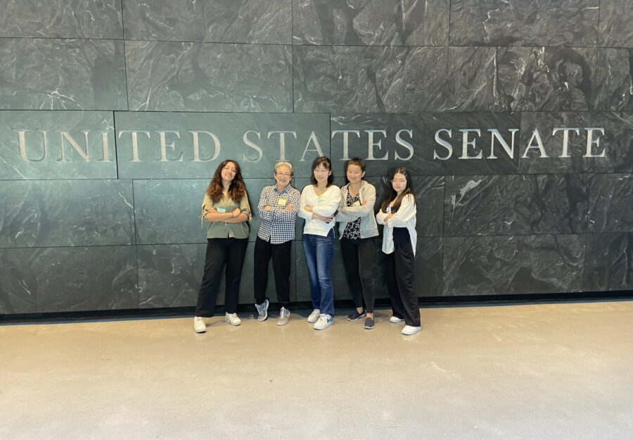 five people stand with arms crossed in front of "United States Senate" sign