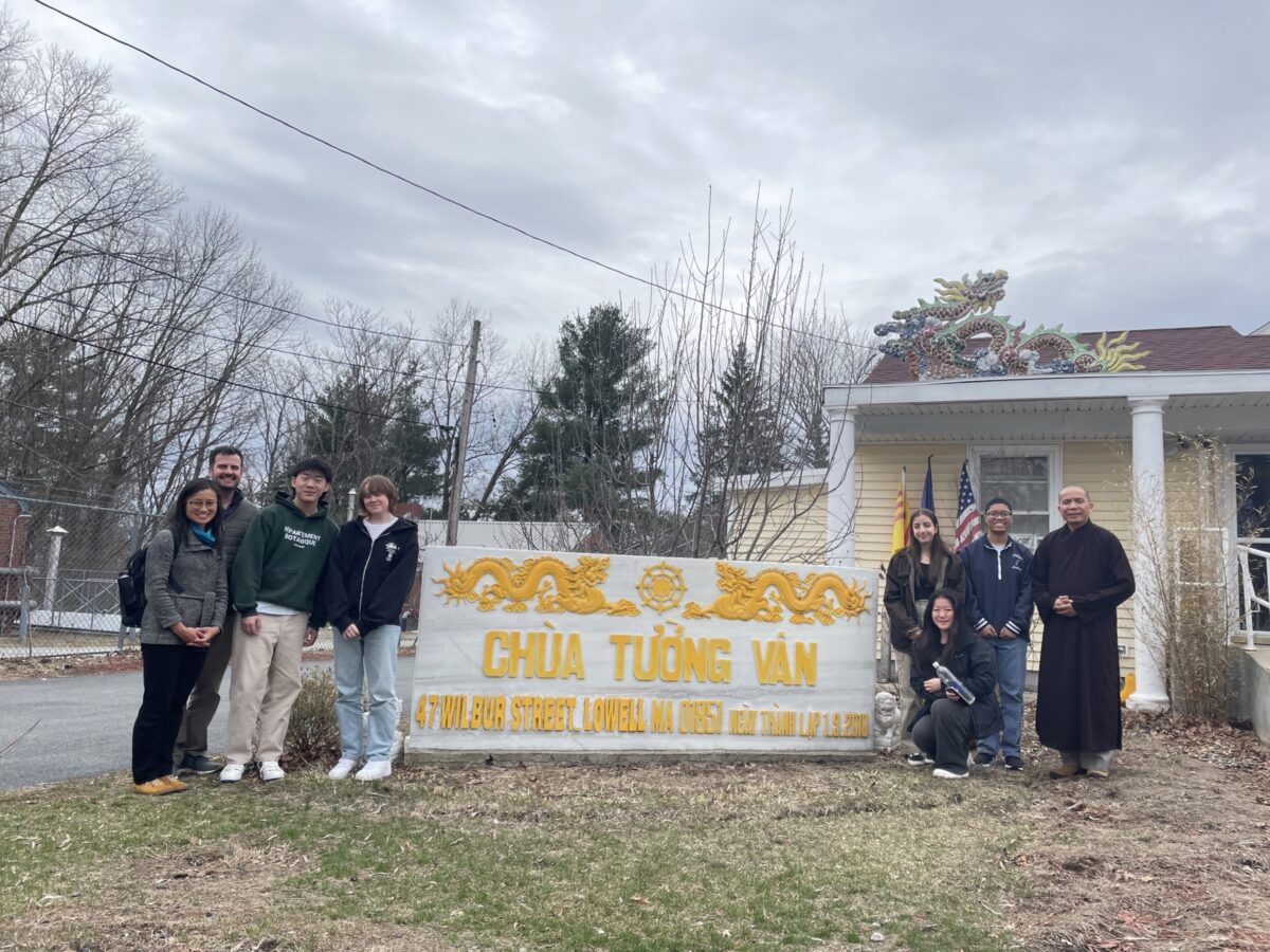 a group of high school students stands outside around the sign at a Buddhist temple