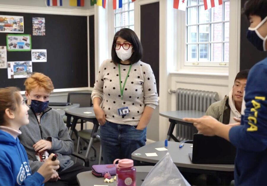 female teacher standing in a classroom surrounded by four students