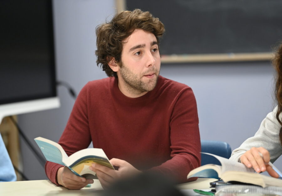 a Caucasian man sitting at a table holding an open book