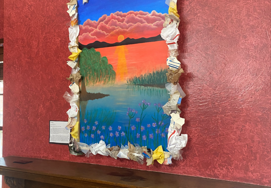 framed painting hanging on a red wall with a brown wooden table beneath