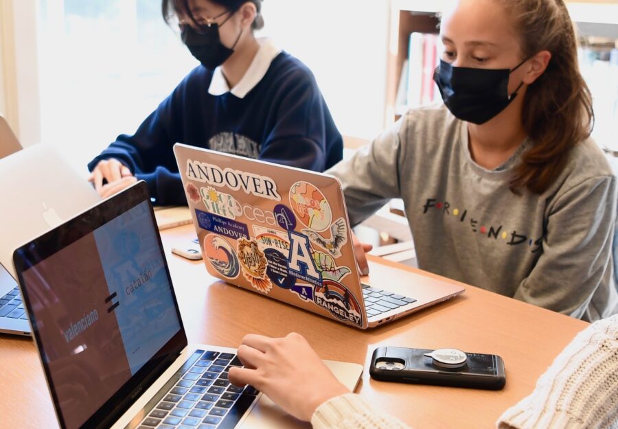 two girls sit at a table with laptops