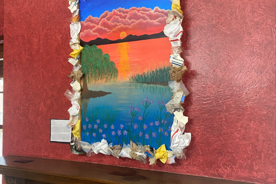 framed painting hanging on a red wall with a brown wooden table beneath