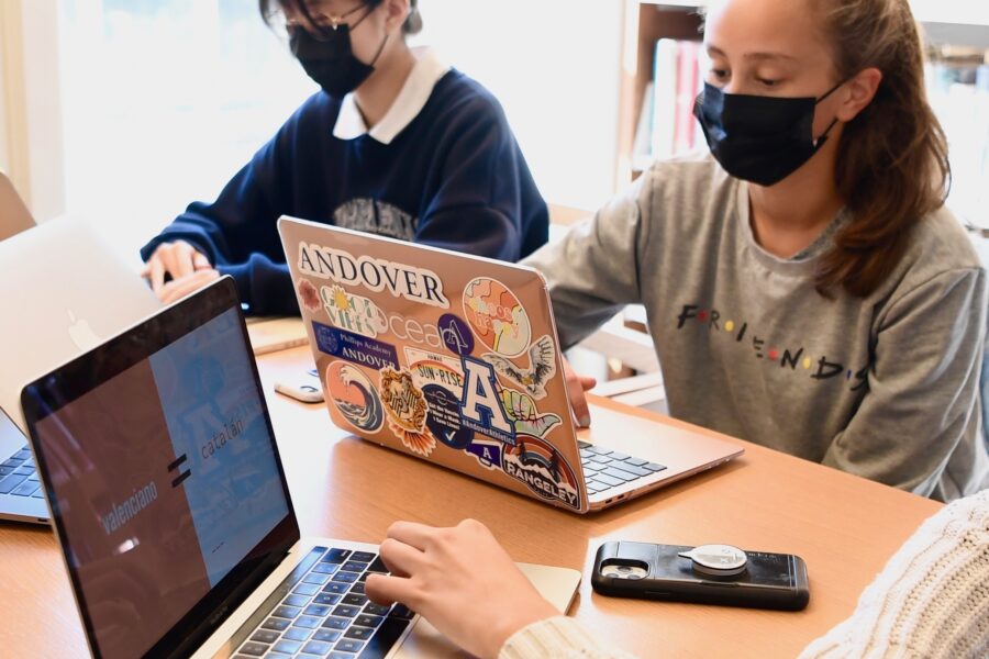 two girls sit at a table with laptops