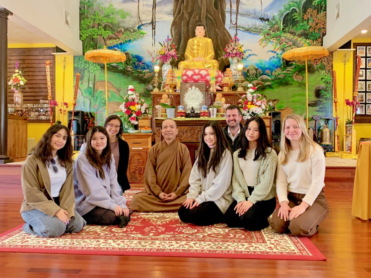 a small group of Workshop students and two teachers kneel on the ground in a temple, all are smiling