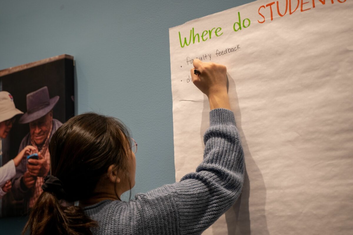 a student writes an idea on a large piece of paper on a wall