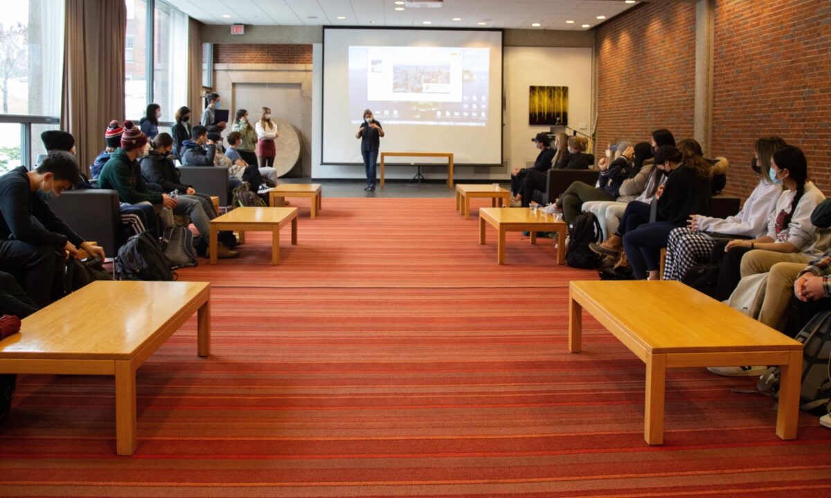 twenty or so students gathered in large room with an orange rug and a white board